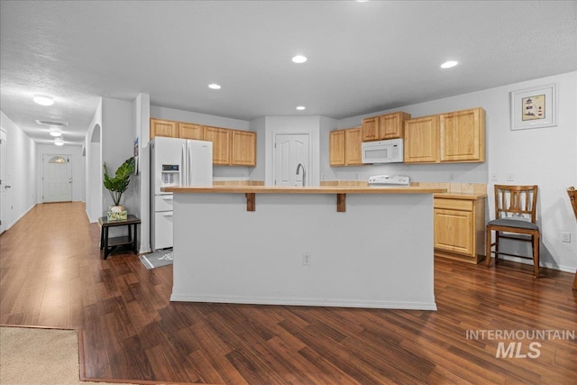 kitchen featuring white appliances, dark wood-type flooring, a kitchen breakfast bar, and a center island