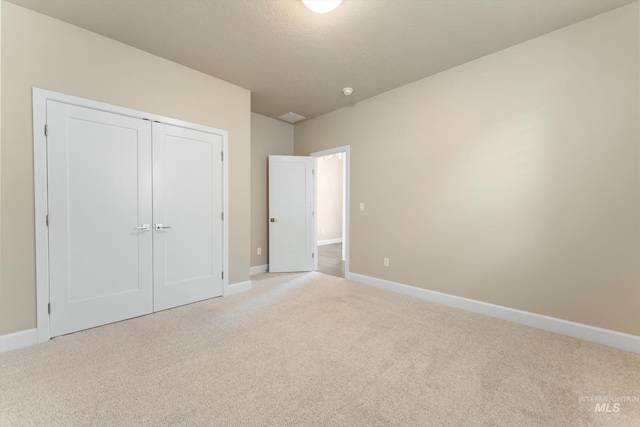 unfurnished bedroom featuring light colored carpet, a textured ceiling, and a closet