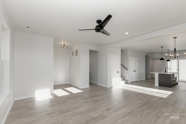 2827 N Rocky Bottom Way, Kuna, ID 83634 - unfurnished living room featuring a sink, ceiling fan, baseboards, stairway, and light wood-type flooring
