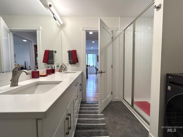 full bathroom featuring double vanity, washer / dryer, a stall shower, and a sink