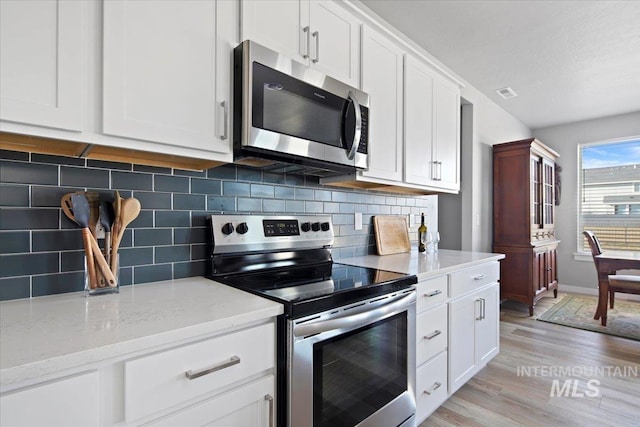 kitchen featuring light wood-type flooring, tasteful backsplash, light stone counters, stainless steel appliances, and white cabinets