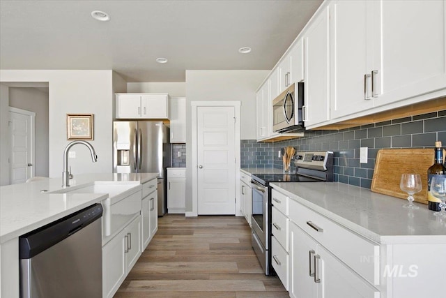 kitchen with white cabinetry, light stone countertops, stainless steel appliances, backsplash, and light wood-type flooring