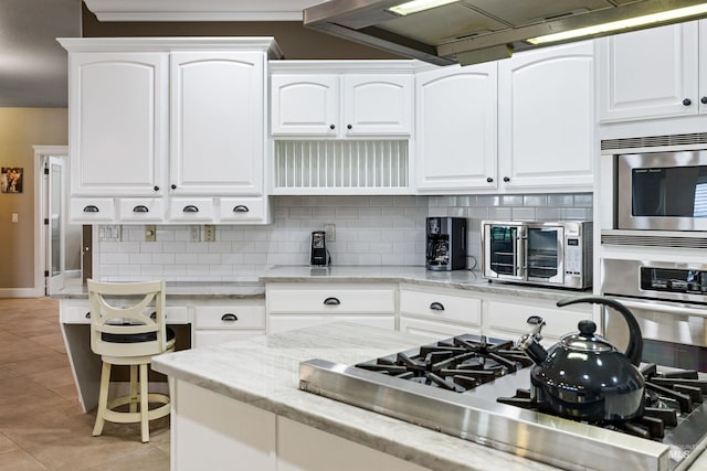 kitchen featuring light stone counters, white cabinets, light tile patterned floors, backsplash, and appliances with stainless steel finishes