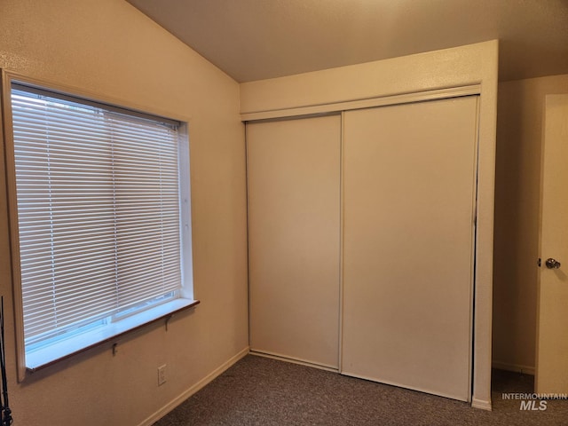 unfurnished bedroom with dark colored carpet, a closet, and lofted ceiling