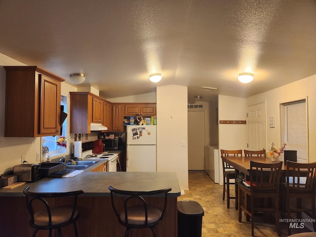 kitchen featuring white appliances, vaulted ceiling, a textured ceiling, kitchen peninsula, and washer / clothes dryer