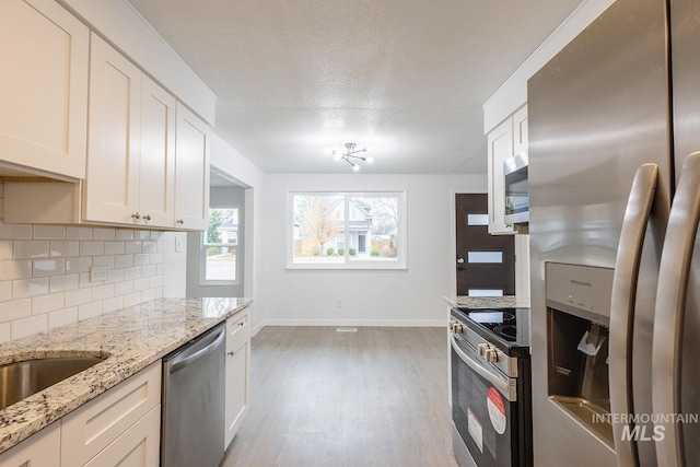 kitchen with light wood-type flooring, appliances with stainless steel finishes, light stone countertops, decorative backsplash, and white cabinets