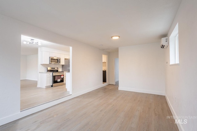 unfurnished room with a wall unit AC and light hardwood / wood-style floors