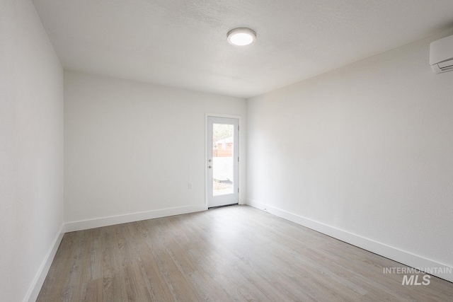 unfurnished room with a textured ceiling, light hardwood / wood-style flooring, and a wall mounted AC