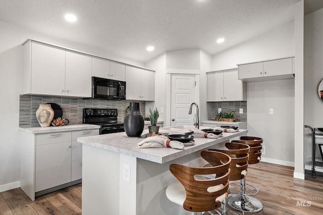 kitchen featuring black appliances, light countertops, vaulted ceiling, light wood-style floors, and a textured ceiling