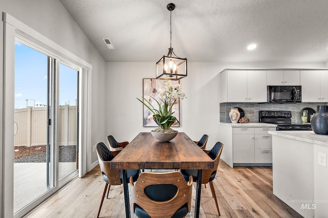 dining area featuring baseboards, visible vents, light wood-style floors, a textured ceiling, and a notable chandelier