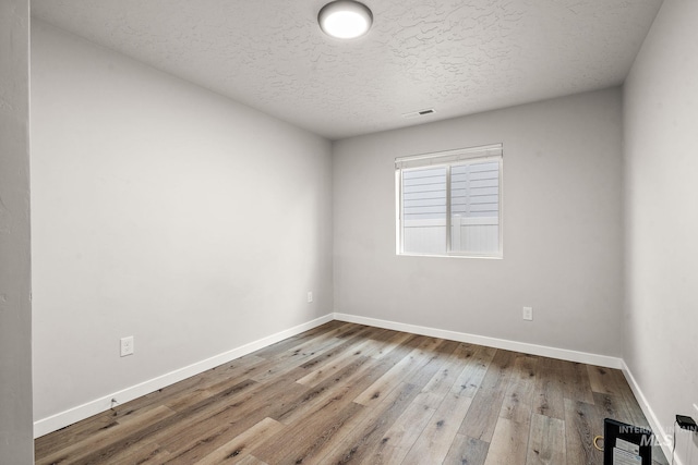 empty room with visible vents, a textured ceiling, baseboards, and wood finished floors