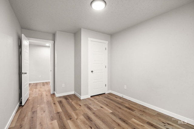 unfurnished bedroom featuring light wood-style floors, baseboards, and a textured ceiling