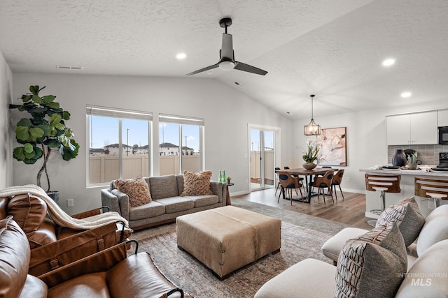 living area featuring visible vents, a textured ceiling, light wood finished floors, lofted ceiling, and ceiling fan