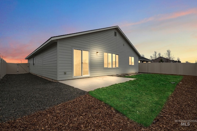 back of property at dusk with a patio area, a lawn, a fenced backyard, and a gate