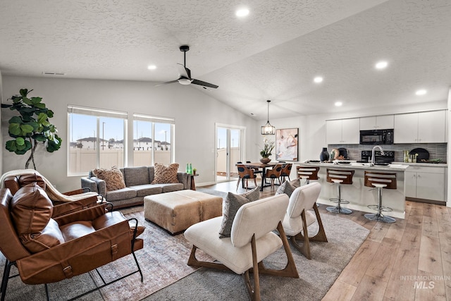 living area with ceiling fan, a wealth of natural light, light wood-style flooring, and vaulted ceiling