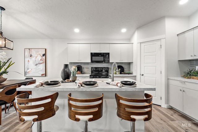 kitchen featuring black appliances, backsplash, light countertops, and light wood finished floors