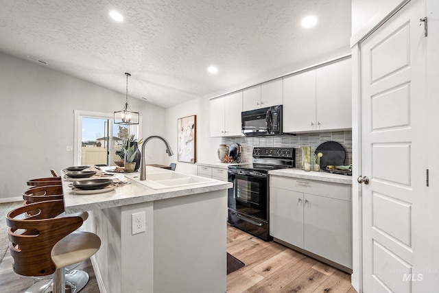 kitchen featuring black appliances, a sink, light wood-style floors, decorative backsplash, and vaulted ceiling