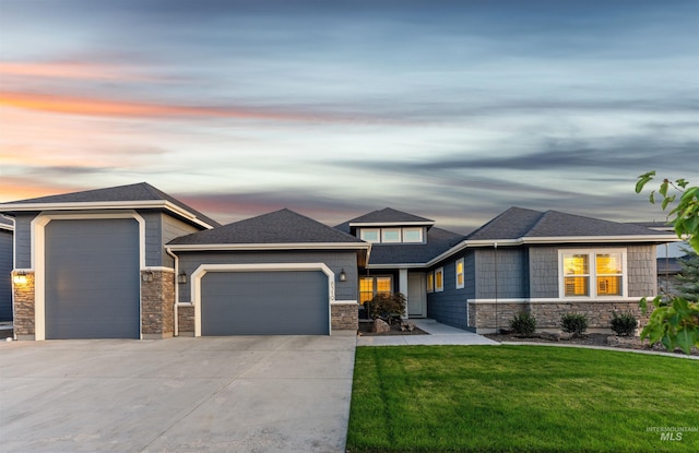 prairie-style home featuring roof with shingles, concrete driveway, a front yard, a garage, and stone siding