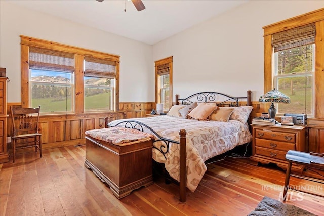 bedroom featuring ceiling fan, light wood-type flooring, multiple windows, and wood walls