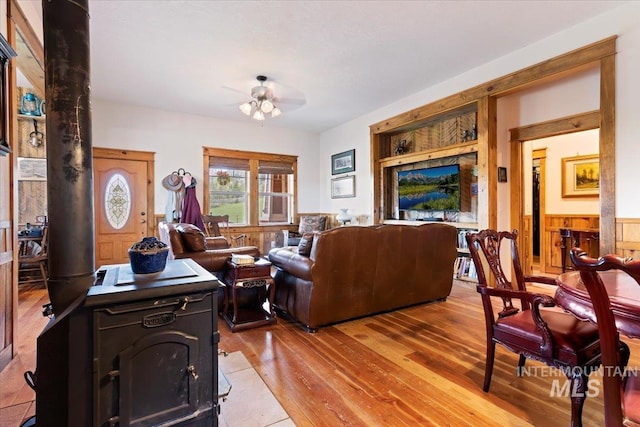 living room featuring hardwood / wood-style flooring, wood walls, ceiling fan, and a wood stove