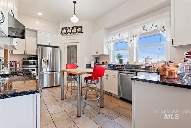 kitchen with decorative light fixtures, wall chimney range hood, white cabinets, and appliances with stainless steel finishes