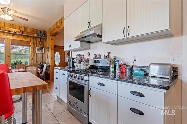 kitchen featuring wooden walls, stainless steel range with gas cooktop, white cabinets, light tile patterned floors, and dark stone counters