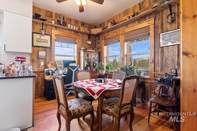 dining area with ceiling fan, light wood-type flooring, and wooden walls