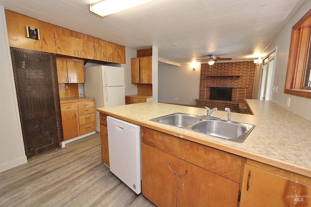 kitchen featuring white appliances, light countertops, light wood-style floors, a fireplace, and a sink