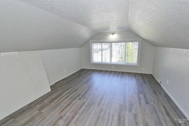 bonus room featuring a textured ceiling, visible vents, baseboards, vaulted ceiling, and dark wood-style floors