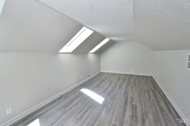 additional living space featuring a textured ceiling, vaulted ceiling with skylight, wood finished floors, visible vents, and baseboards