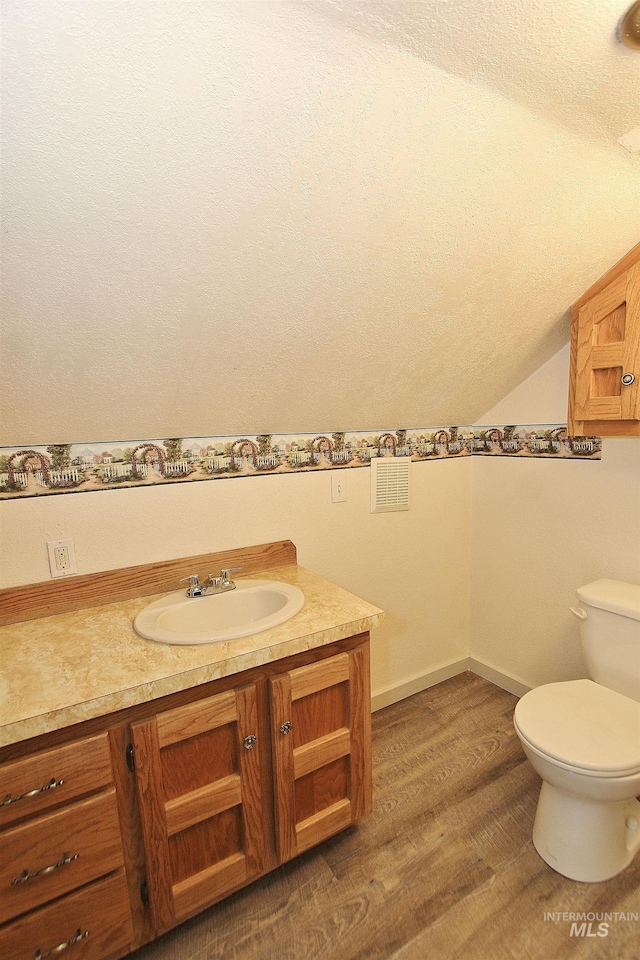 bathroom featuring lofted ceiling, a textured ceiling, toilet, wood finished floors, and vanity