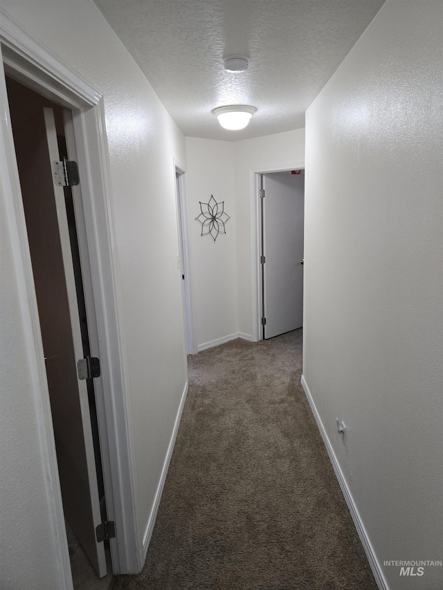 hallway featuring carpet floors, baseboards, and a textured ceiling