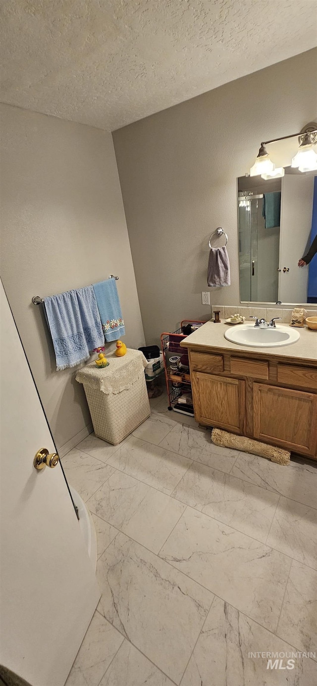 bathroom featuring marble finish floor, a shower, a textured ceiling, and vanity