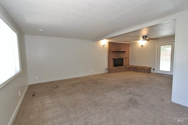 unfurnished living room with carpet floors, a brick fireplace, ceiling fan, and visible vents