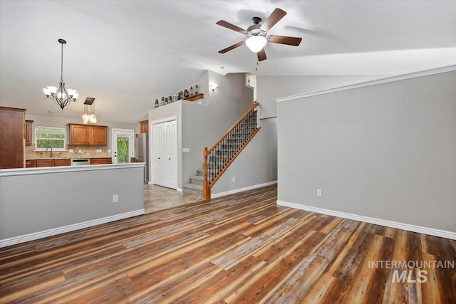 unfurnished living room with ceiling fan with notable chandelier, vaulted ceiling, and dark hardwood / wood-style flooring