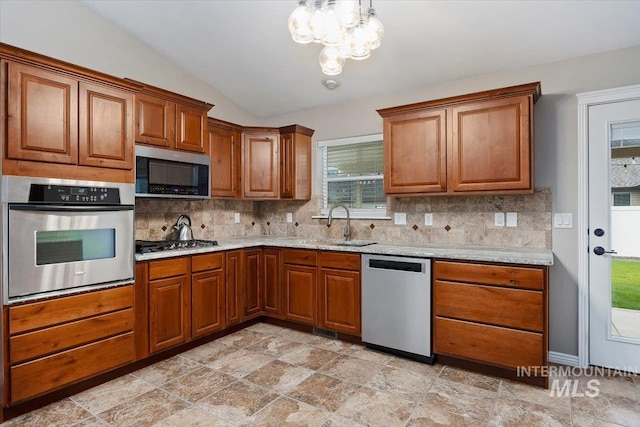 kitchen with tasteful backsplash, light stone countertops, appliances with stainless steel finishes, hanging light fixtures, and lofted ceiling