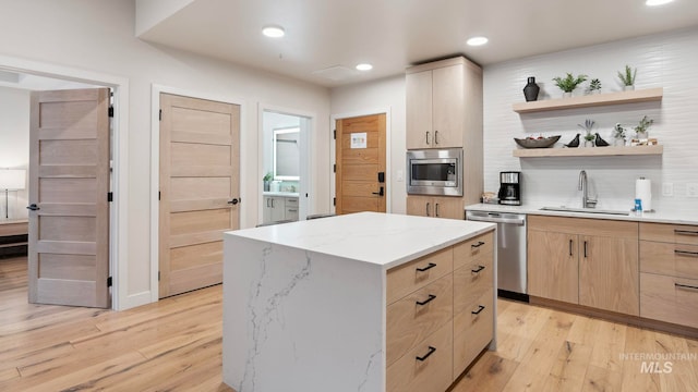 kitchen with light brown cabinetry, sink, appliances with stainless steel finishes, light wood-type flooring, and a center island