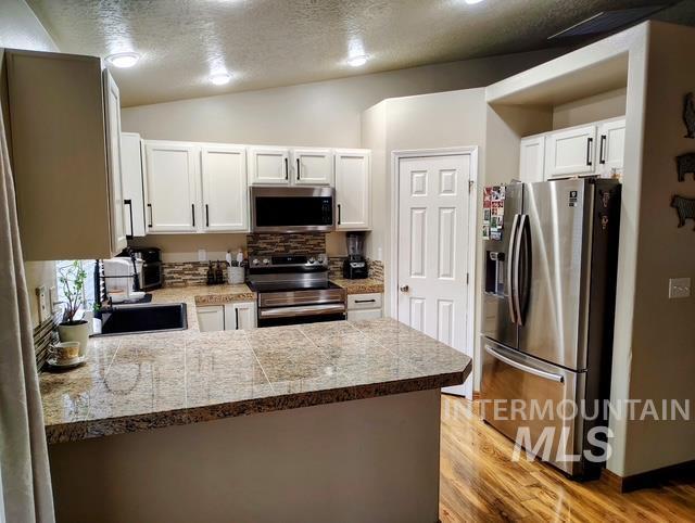 2150 W Shy Crk, Nampa, ID 83686 - kitchen featuring appliances with stainless steel finishes, tile countertops, light wood finished floors, a sink, and white cabinetry
