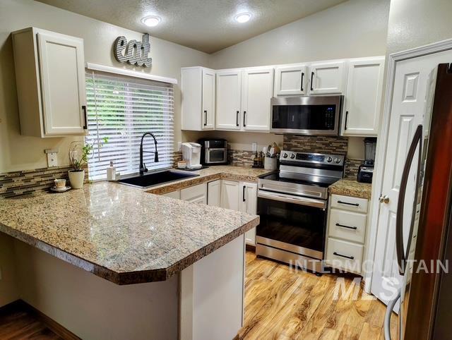 2150 W Shy Crk, Nampa, ID 83686 - kitchen with appliances with stainless steel finishes, a sink, a peninsula, white cabinetry, and lofted ceiling