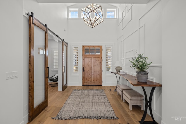 entrance foyer featuring a towering ceiling, an inviting chandelier, a barn door, and wood finished floors