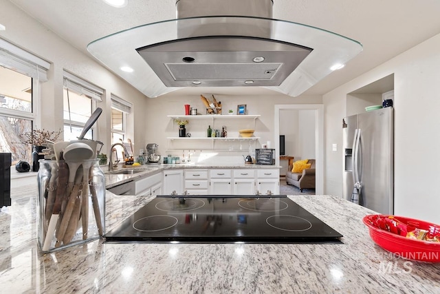 kitchen featuring black electric stovetop, light stone countertops, stainless steel refrigerator with ice dispenser, white cabinets, and sink