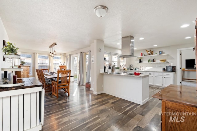 kitchen with kitchen peninsula, a textured ceiling, island range hood, hanging light fixtures, and white cabinetry