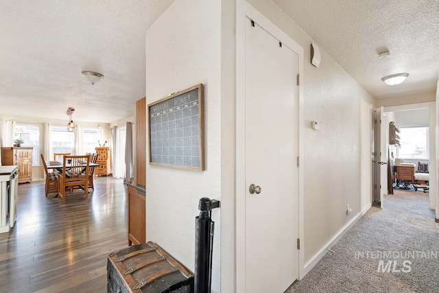 corridor featuring a textured ceiling and dark colored carpet