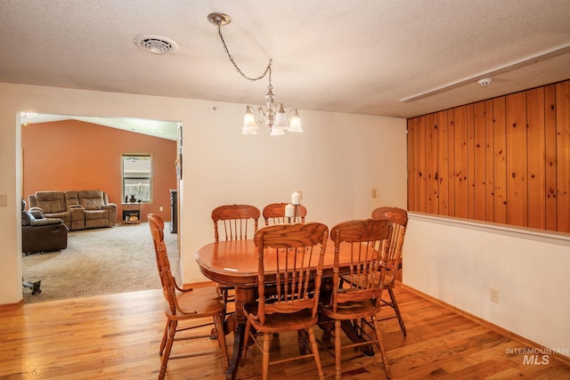 dining space with an inviting chandelier, a textured ceiling, light wood-type flooring, and wooden walls