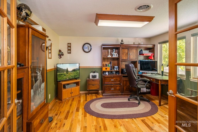 home office with light hardwood / wood-style flooring and a textured ceiling