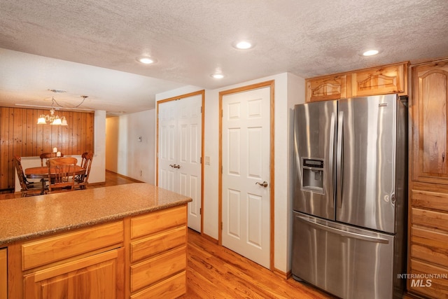 kitchen featuring a chandelier, light wood-type flooring, pendant lighting, stainless steel fridge with ice dispenser, and a textured ceiling