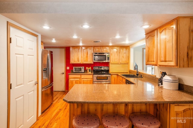 kitchen featuring sink, kitchen peninsula, a textured ceiling, light hardwood / wood-style flooring, and stainless steel appliances