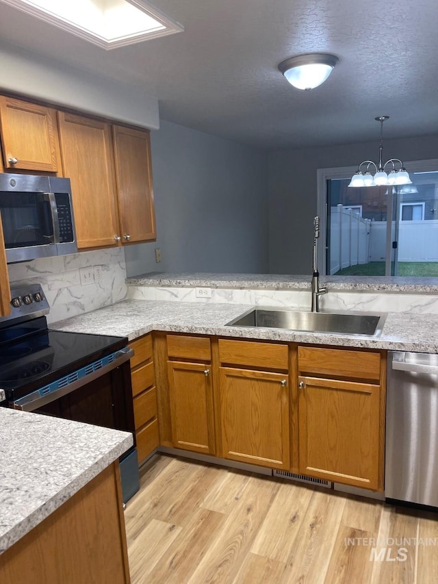 kitchen featuring sink, stainless steel appliances, tasteful backsplash, light hardwood / wood-style flooring, and decorative light fixtures