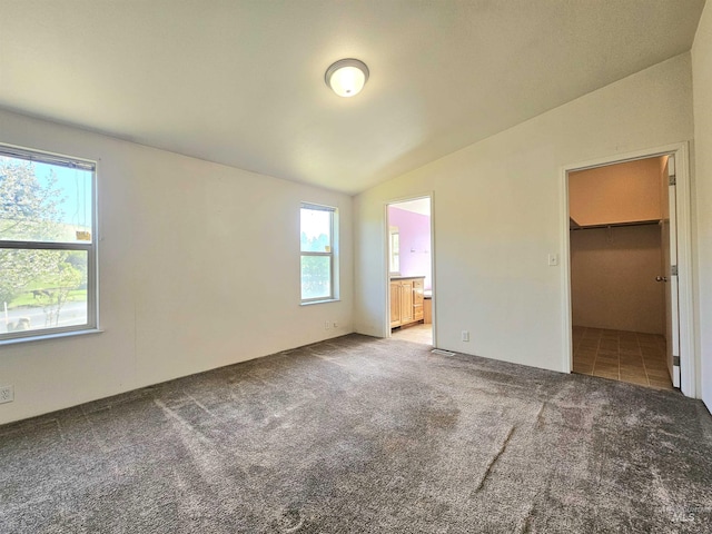 unfurnished bedroom featuring vaulted ceiling, carpet, a walk in closet, and ensuite bathroom