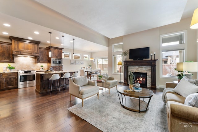 living room featuring a stone fireplace, recessed lighting, dark wood-style floors, and baseboards